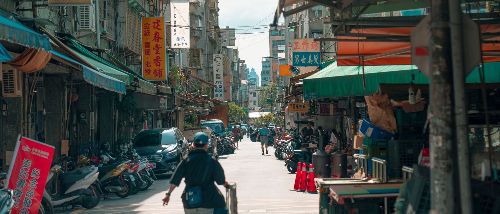 白天的台灣街道，兩旁是騎樓、遮陽棚與在地小店的招牌。